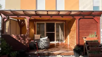 Überdachte Holzterrasse mit Sitzgelegenheiten und Zugang zum kleinen Gartenbereich hinter dem Reihenhaus.