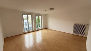 Heller Raum mit Holzboden, Heizkörper und zwei Fenstern mit französischen Balkonen.
