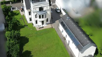 Luftaufnahme eines weißen Gebäudes mit großem Rasen, umgeben von Bäumen und ländlicher Umgebung.