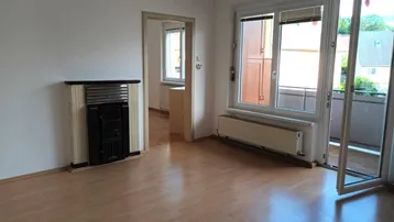 Helles Wohnzimmer mit Laminatboden, Kachelofen und Zugang zu einem Balkon.