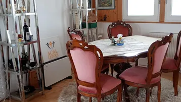 Gemütlicher Essbereich mit traditionellen Holzmöbeln, rosa Stühlen und sichtbaren Deckenbalken unter Dachschräge.