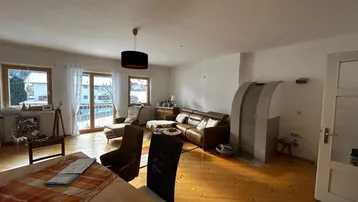 Geräumiger Wohn-Essbereich mit Holzboden, gemütlicher Sitzecke und einem traditionellen Kaminofen.