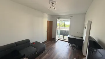 Helles Wohnzimmer mit dunklem Laminatboden, Sofa und Zugang zu einem Balkon.