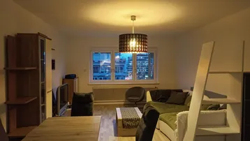 Gemütlicher Wohn- und Essbereich mit Parkettboden, Sofa und Blick auf die Stadt bei Nacht.