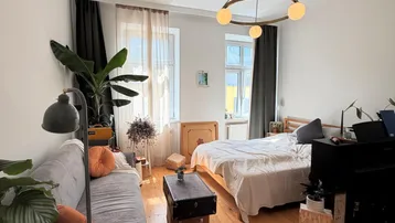 Helles und gemütliches Wohnzimmer mit Holzboden, Sofa, Bett und einem modernen Kronleuchter.