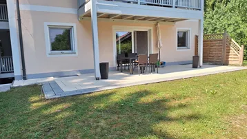 Erdgeschoss-Terrasse mit Gartenmöbeln und Zugang zum Garten, darüber ein Balkon.