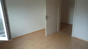 Helles Zimmer mit Laminatboden und einer offenen Tür zu einem weiteren Raum.