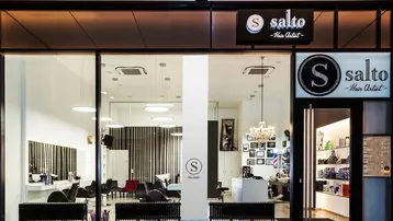 Moderne Friseursalon-Fassade mit großen Glasfenstern, die den stilvollen Innenbereich zeigen und viel Licht hereinlassen.