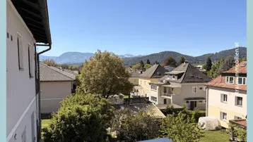 Weitblick über die Dächer der Nachbarschaft mit grünen Bäumen und Bergen im Hintergrund.