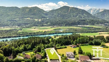 Luftaufnahme eines Grundstücks in ländlicher Umgebung mit Bergen, Fluss und Wäldern im Hintergrund.