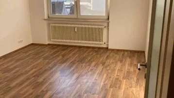 Helles Zimmer mit Laminatboden und Heizkörper unter dem Fenster, bietet einen Blick auf die Umgebung.