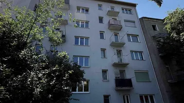 Fassade eines Mehrfamilienhauses mit mehreren Balkonen unter strahlendem Sonnenschein.