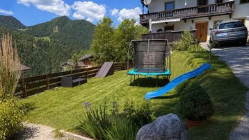 Großer Garten mit Trampolin, Rutsche und herrlichem Bergblick, ideal für Familien.