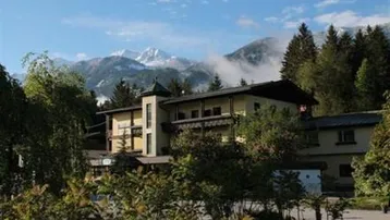 Gebäude mit alpiner Architektur, umgeben von Bäumen und mit beeindruckendem Bergblick auf schneebedeckte Gipfel.