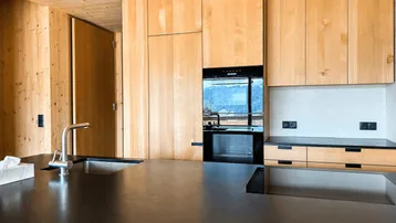Moderne Holzküche mit dunkler Arbeitsplatte, integrierten Geräten und Bergblick.