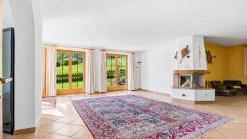 Geräumiges Wohnzimmer mit Kamin, Fliesenboden und Zugang zum Garten durch große Fenstertüren.