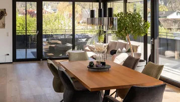 Heller Wohn- und Essbereich mit Holzboden, großen Glasfronten und Zugang zur Terrasse.