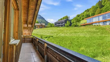 Balkon mit Holzbalkon und weitem Blick über grüne Felder und moderne Gebäude in der Ferne.