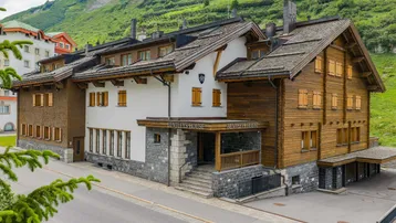 Traditionelles Holz- und Steingebäude im alpinen Stil mit Blick auf die umliegende Berglandschaft.