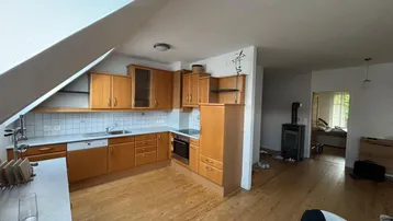 Geräumige Küche mit Holzschränken, integrierten Geräten und einem gemütlichen Holzofen im offenen Wohnbereich.