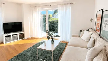 Helles Wohnzimmer mit beigem Sofa, Holzboden und Zugang zu einem sonnigen Balkon.