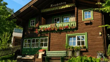 Traditionelles Holzhaus mit grünen Fensterläden und Blumenkästen unter blauem Himmel.