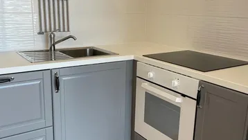 Funktionale Küchenzeile mit grauen Unterschränken, Spüle, Induktionskochfeld und Backofen.