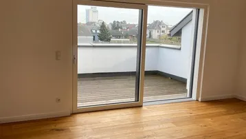Lichtdurchfluteter Raum mit Holzboden und Zugang zu einer Terrasse mit weitem Blick.