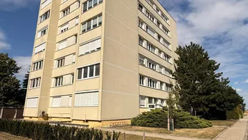 Mehrstöckiges Wohngebäude mit heller Fassade und vielen Fenstern unter blauem Himmel.