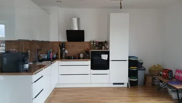 Moderne Küche mit weißen Schränken, Holzarbeitsplatte und integrierten Geräten.