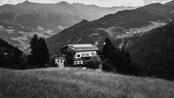 Ein Haus mit Solarpaneelen auf dem Dach, eingebettet in eine weite Berglandschaft mit grünen Wiesen.
