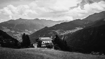 Schwarz-Weiß-Aufnahme eines Hauses mit Solarpaneelen auf dem Dach, eingebettet in eine weite Berglandschaft.
