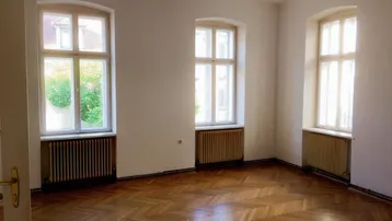 Heller Wohnraum mit klassischem Fischgrätparkett, hohen Fenstern und Blick ins Grüne.