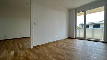 Geräumiges Wohnzimmer mit Parkettboden und Zugang zu einem französischen Balkon.