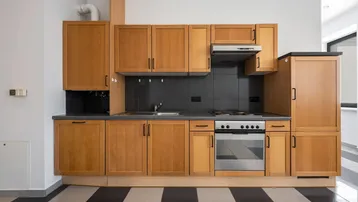 Funktionale Küche mit Holzschränken, dunkler Arbeitsplatte und markantem schwarz-weißem Fliesenboden.