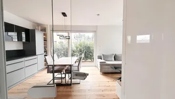 Heller, offener Wohn-Essbereich mit moderner Küche, Holzboden und Zugang zur Terrasse.