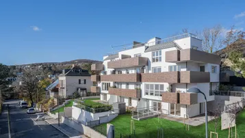 Modernes Mehrfamilienhaus mit Terrassen und Grünflächen in hügeliger Umgebung.