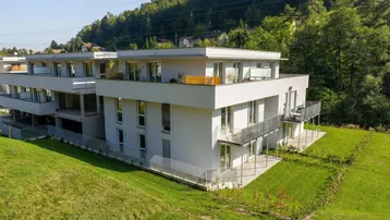 Luftaufnahme eines modernen Wohnkomplexes mit Flachdächern und Balkonen, eingebettet in eine grüne Hügellandschaft.