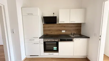 Moderne Einbauküche mit weißen Schränken, Holzrückwand und integrierten Geräten.