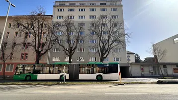 Mehrstöckiges Wohngebäude an einer Straße mit einem Bus davor unter blauem Himmel.