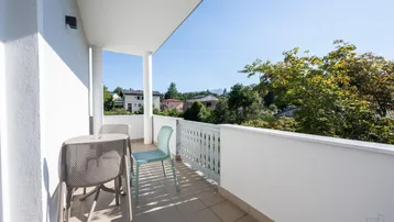 Heller Balkon mit Sitzgelegenheiten und Blick auf die umliegende Wohngegend und Bäume.