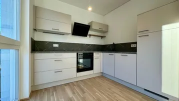 Moderne Küche mit hellgrauen Schränken, dunkler Arbeitsplatte und Holzboden, gut beleuchtet durch ein großes Fenster.
