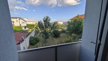 Blick von einem Balkon auf eine grüne Umgebung mit Bäumen und Häusern im Hintergrund.