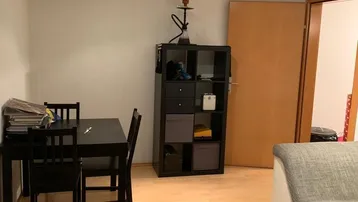 Heller Wohn- und Essbereich mit Laminatboden, Esstisch und Sofa unter einer modernen Schienenbeleuchtung.