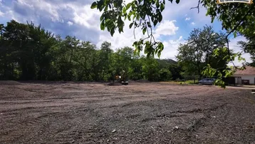 Großes Grundstück in Vorbereitung für den Bau mit Bagger und umliegender Natur unter blauem Himmel.
