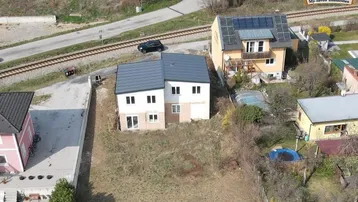 Luftaufnahme eines im Bau befindlichen Hauses mit umliegender Landschaft und Bahngleisen.