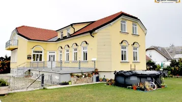 Gelbes Wohnhaus mit rotem Dach, Gartenbereich und kleinem Aufstellpool im Freien.