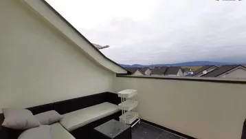 Möblierte Dachterrasse mit Sitzgelegenheiten und weitem Blick über Dächer und Landschaft.