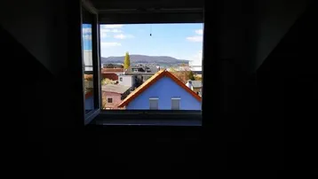 Kleines Fenster in einem dunklen Raum mit Blick auf ein blaues Dach und die umliegende Landschaft.