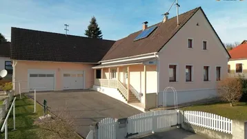 Freistehendes Einfamilienhaus mit beiger Fassade, Satteldach, Doppelgarage und gepflegtem Vorgarten.